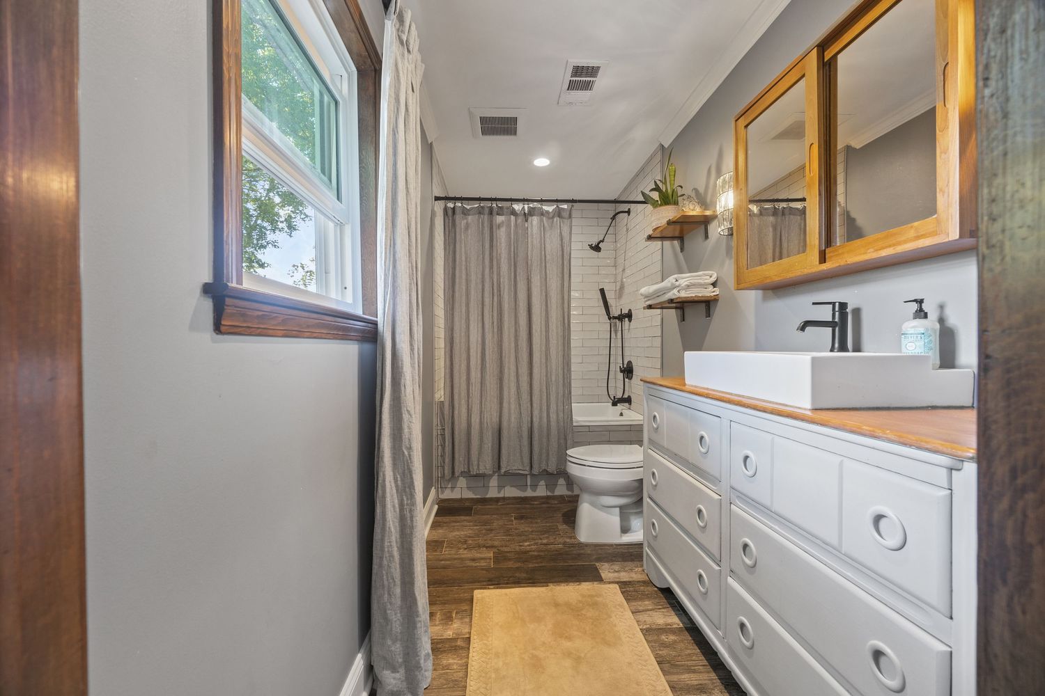 Modern bathroom renovation features white cabinets, wood accents, and elegant fixtures in a long, narrow layout.