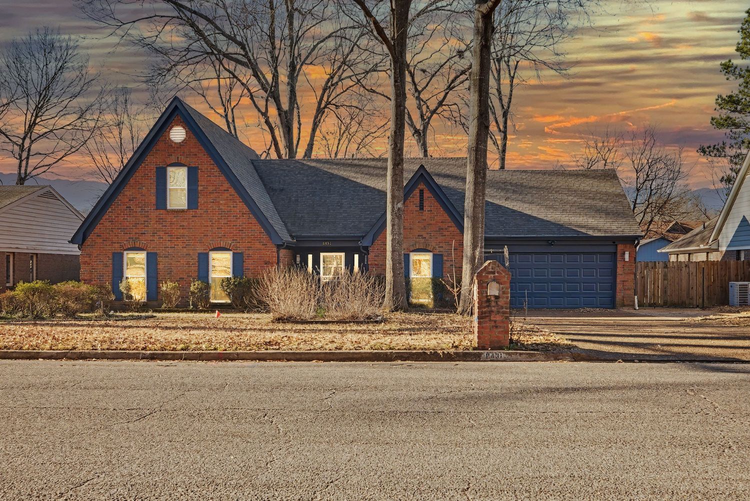 A panoramic view of suburban houses at sunset with bare trees silhouetted against an orange and purple sky.
