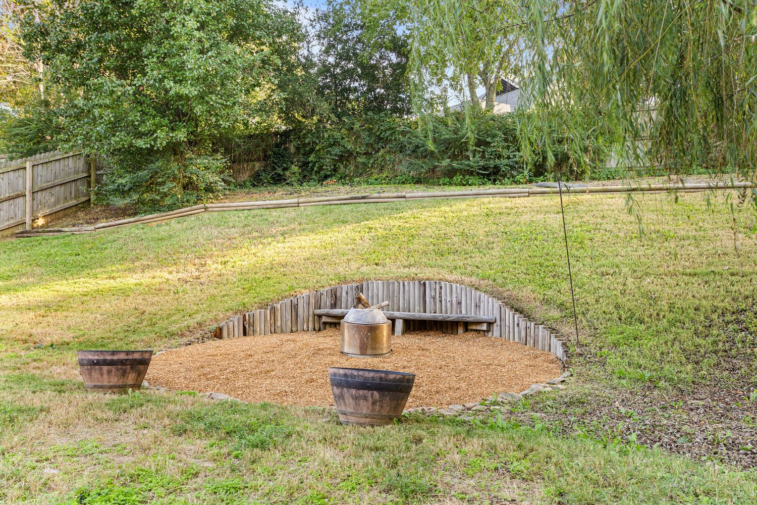 A curved wooden bench sits in a circular mulch area surrounded by a sloping green lawn and garden landscaping.