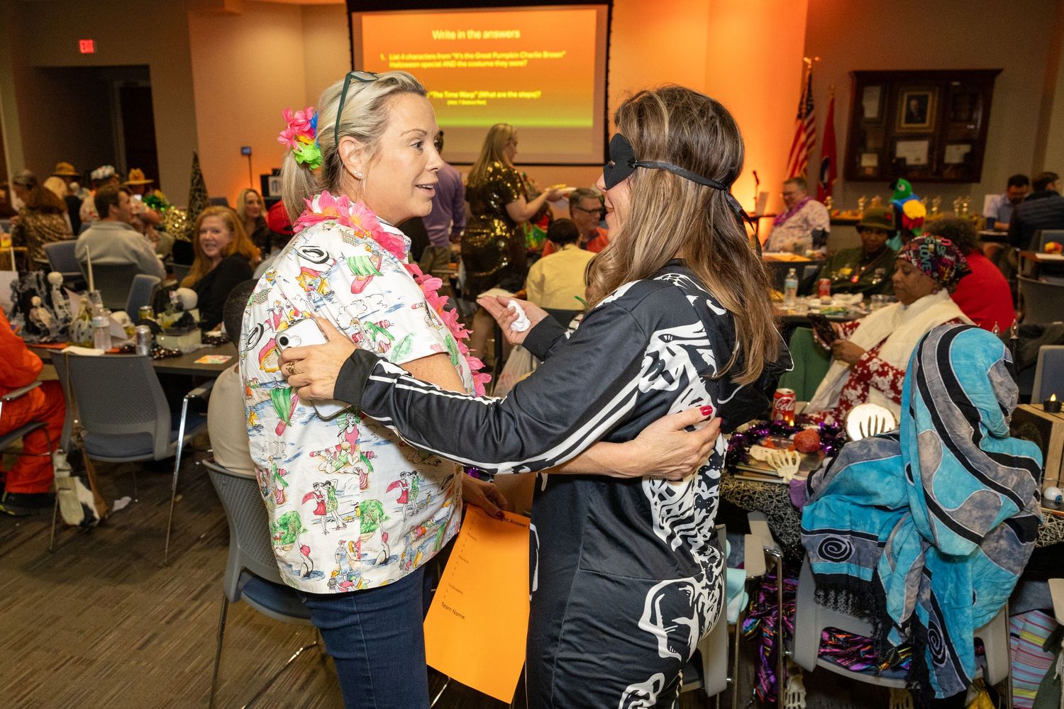 People mingling at an indoor event with decorative lighting and projection screens.