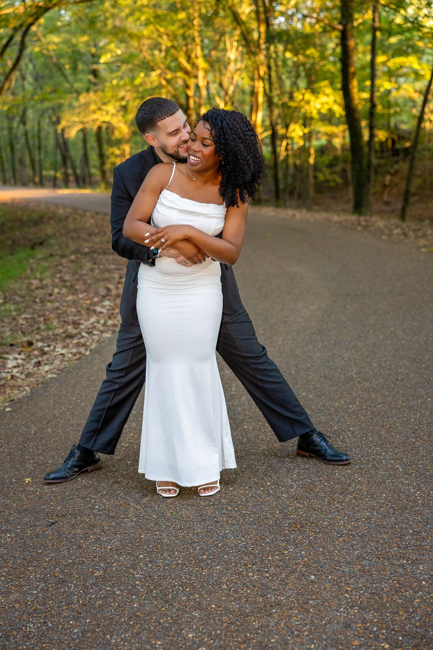 Playful wedding photography poses on a gravel path surrounded by fall foliage.