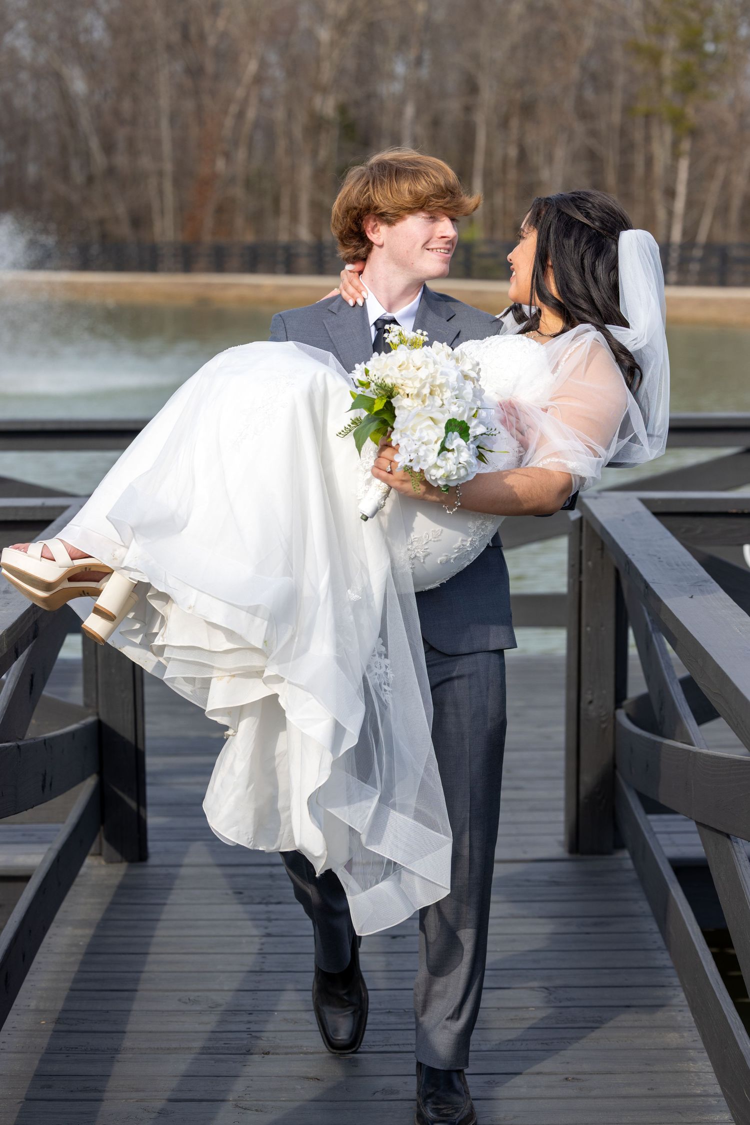 Wedding couple shares romantic dip kisses on a wooden deck overlooking a serene lake.
