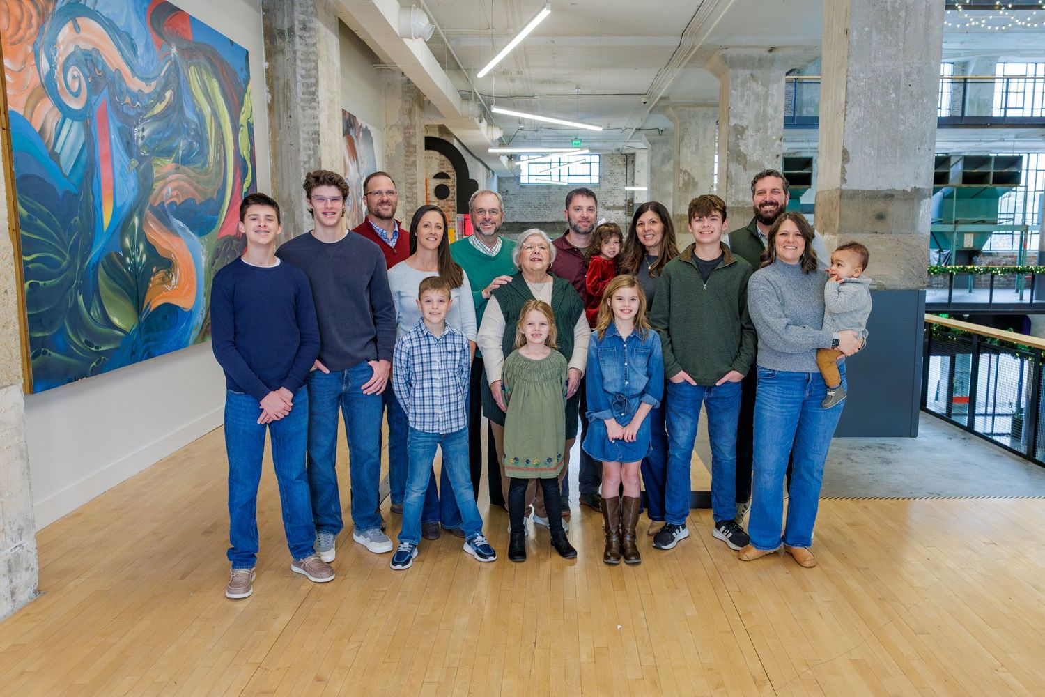 A group of people standing together in a modern office space with a colorful mural on the wall behind them.