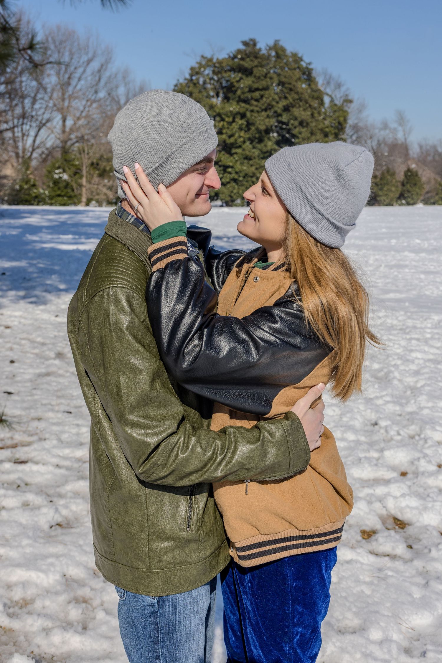 A couple embracing outdoors in winter wearing matching gray beanies.