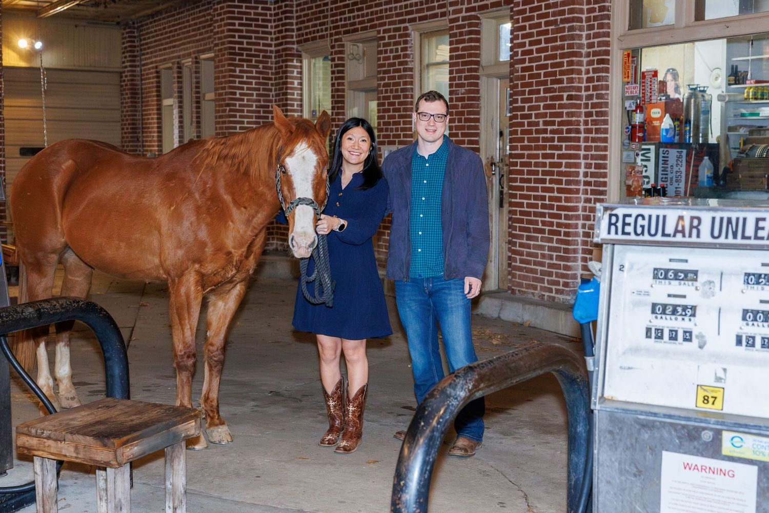 Horse standing inside a brick stable area with posted signs on the wall.