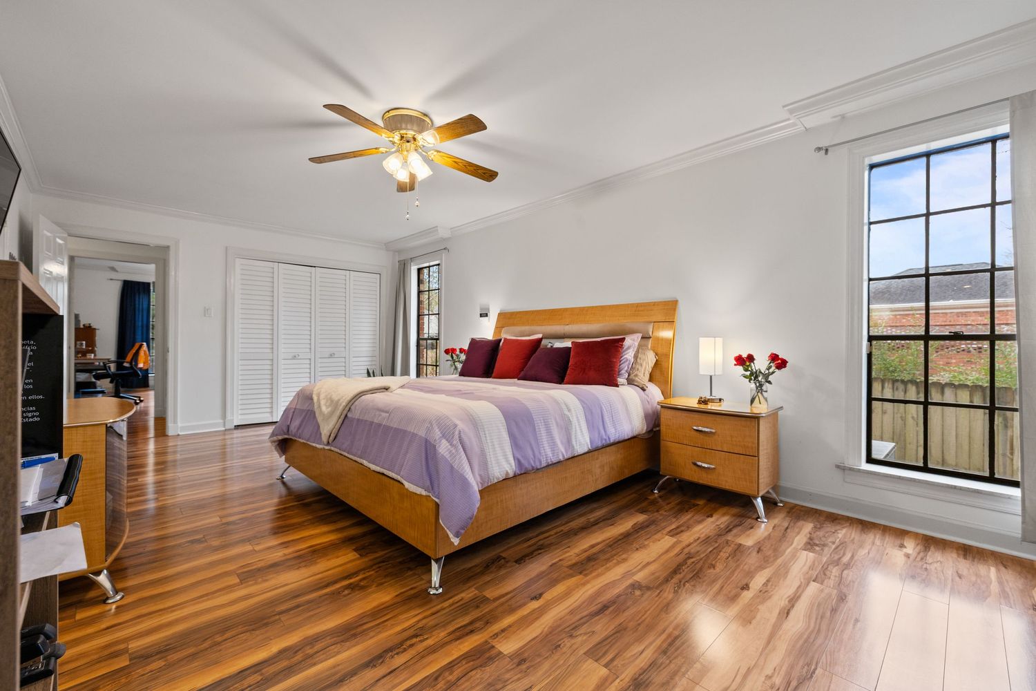 Bright bedroom with hardwood floors, ceiling fan, and large windows.