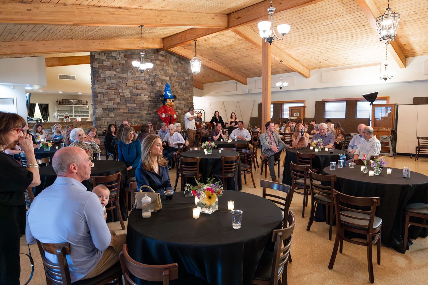 Large group of guests mingling at a decorated event hall with round tables.