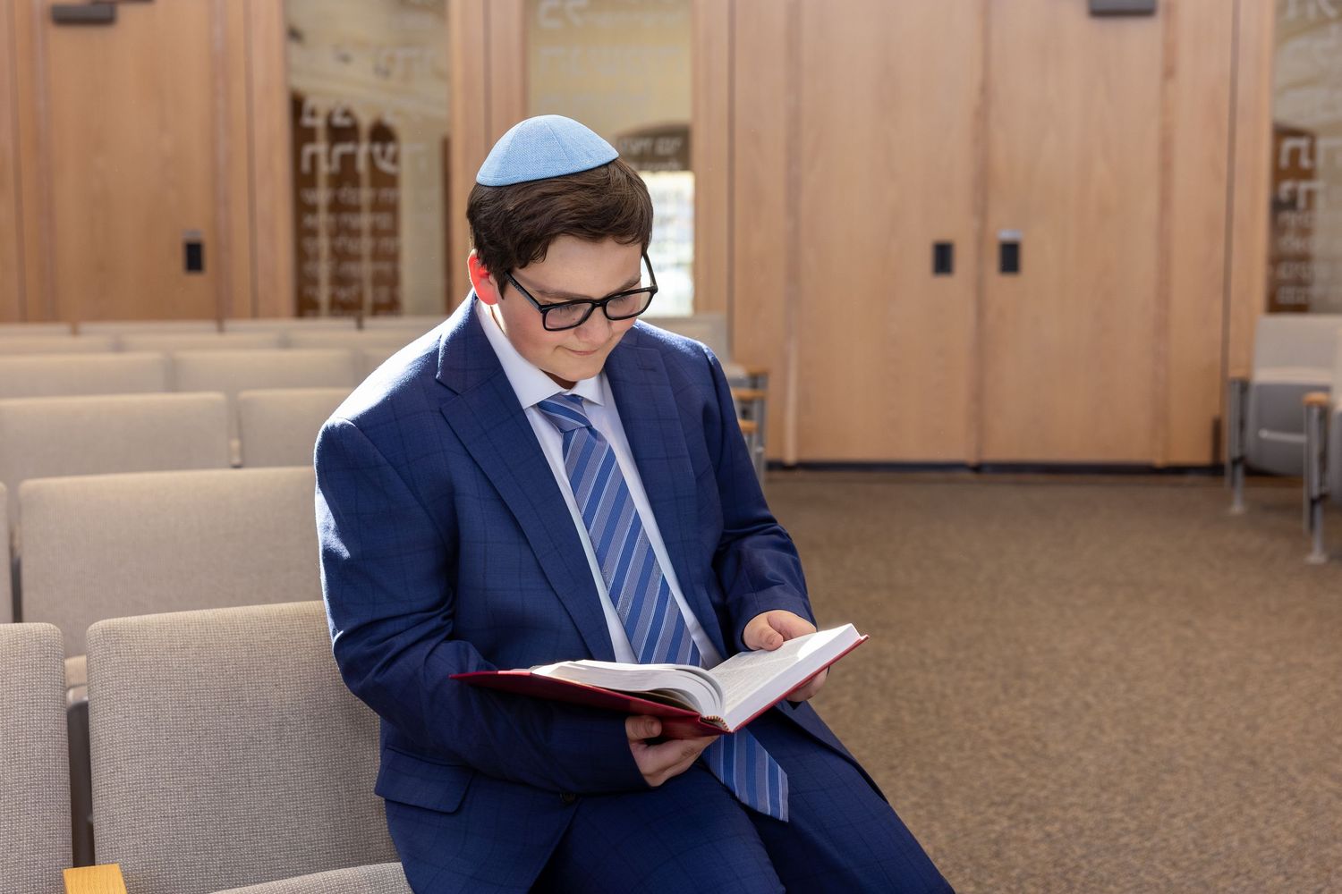 Professional in a navy suit reads through documents while sitting in an office lobby area.