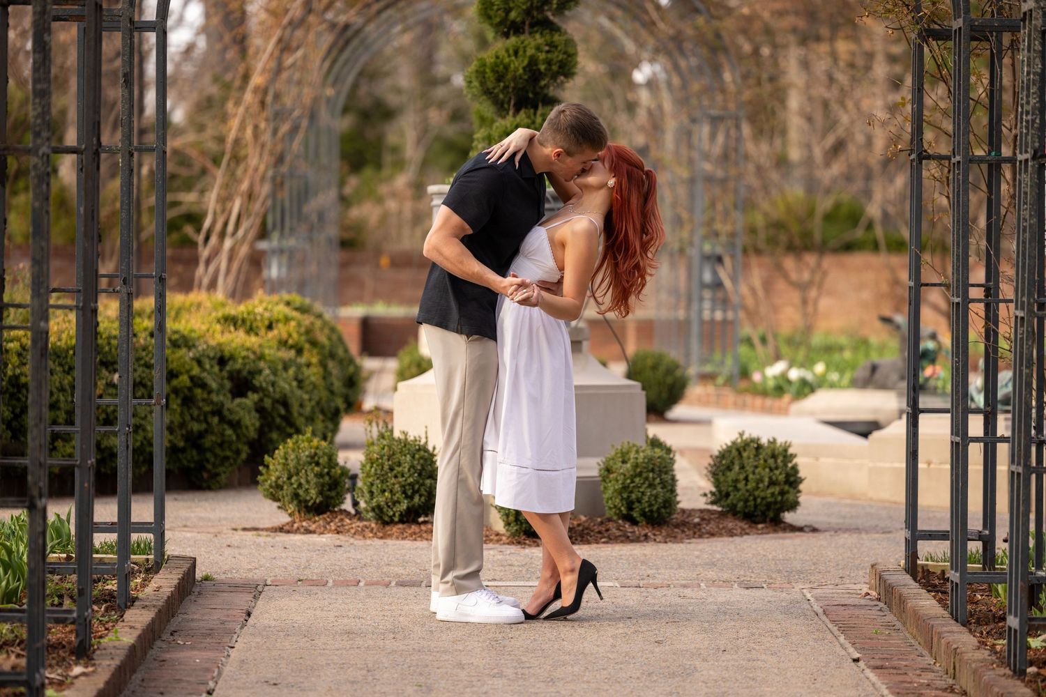 Couple strolling along an ornate garden walkway with decorative metal archways and landscaped borders.