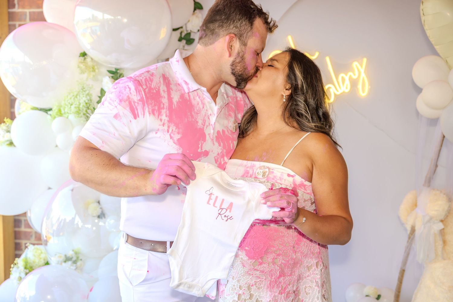 A celebration scene with white balloons and pink confetti against a decorated brick wall.