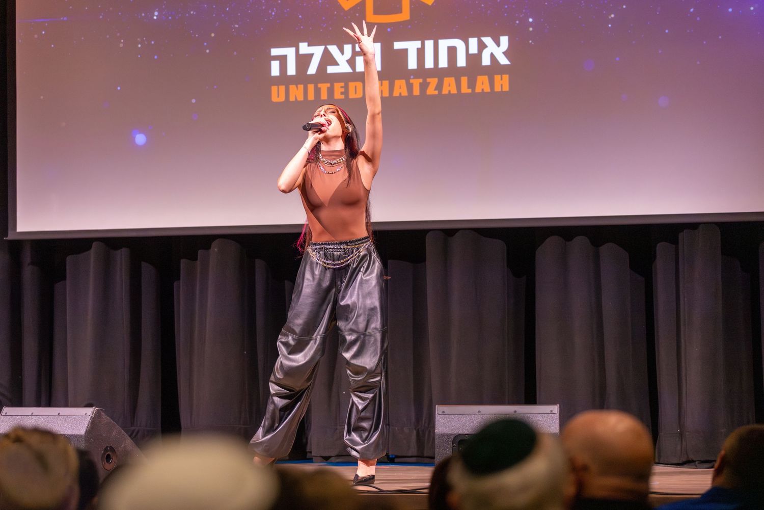 Performer on stage with Hebrew text projected on screen behind them.