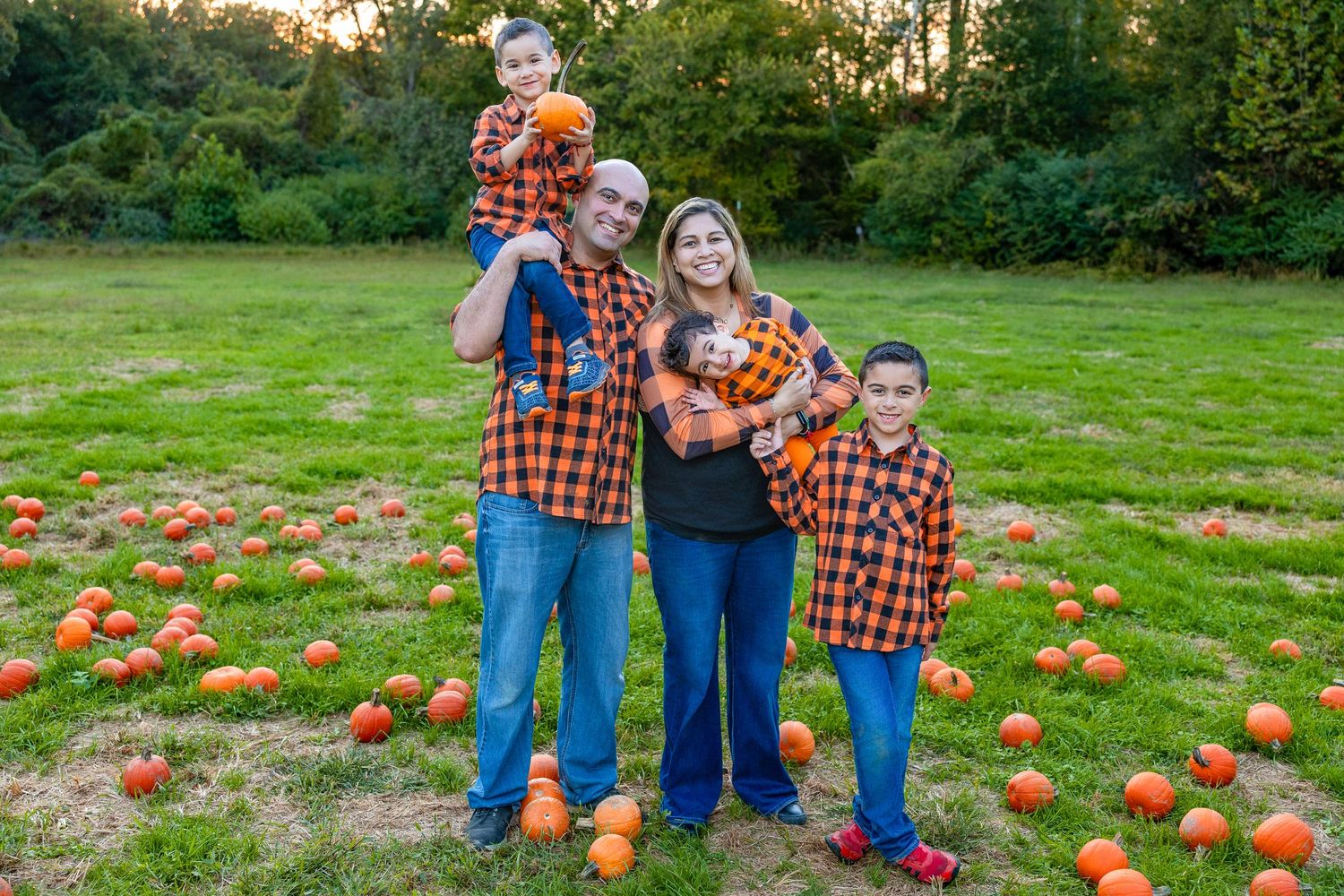 Family in matching plaid shirts poses together in a pumpkin patch during autumn.