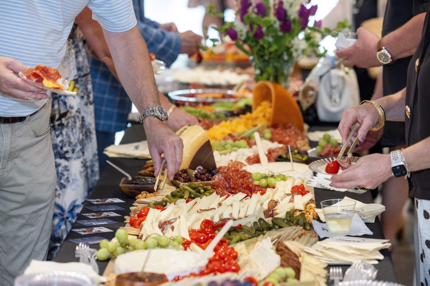 People serving themselves at an elegant buffet spread with cheese, fresh vegetables, and appetizers at a catered event.