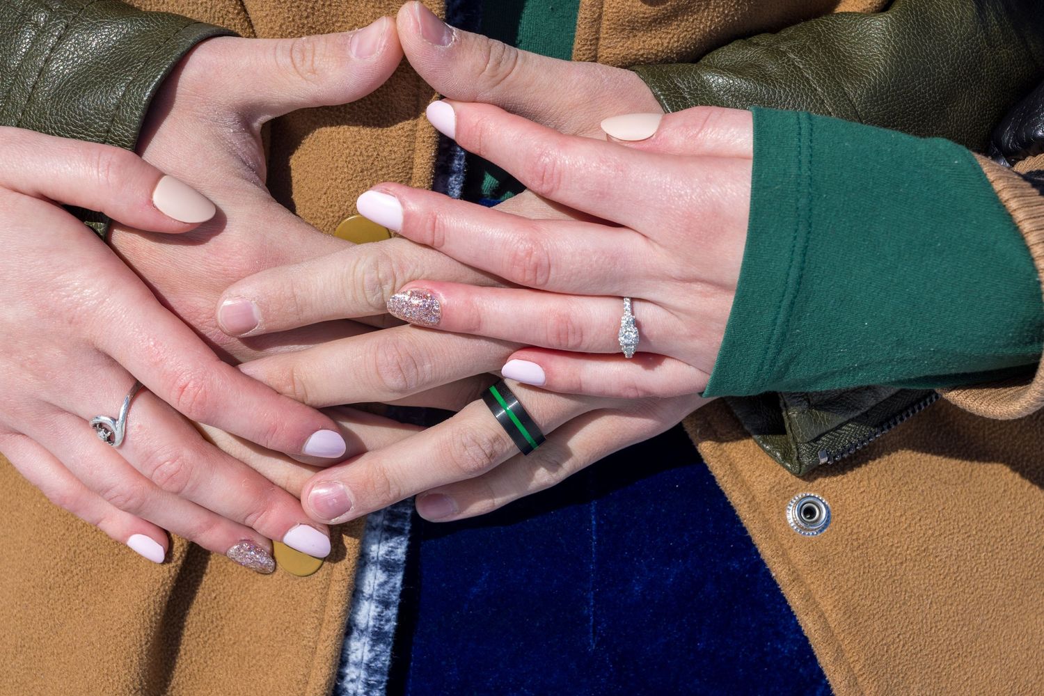 Close-up of hands showing off new engagement rings against winter clothing.