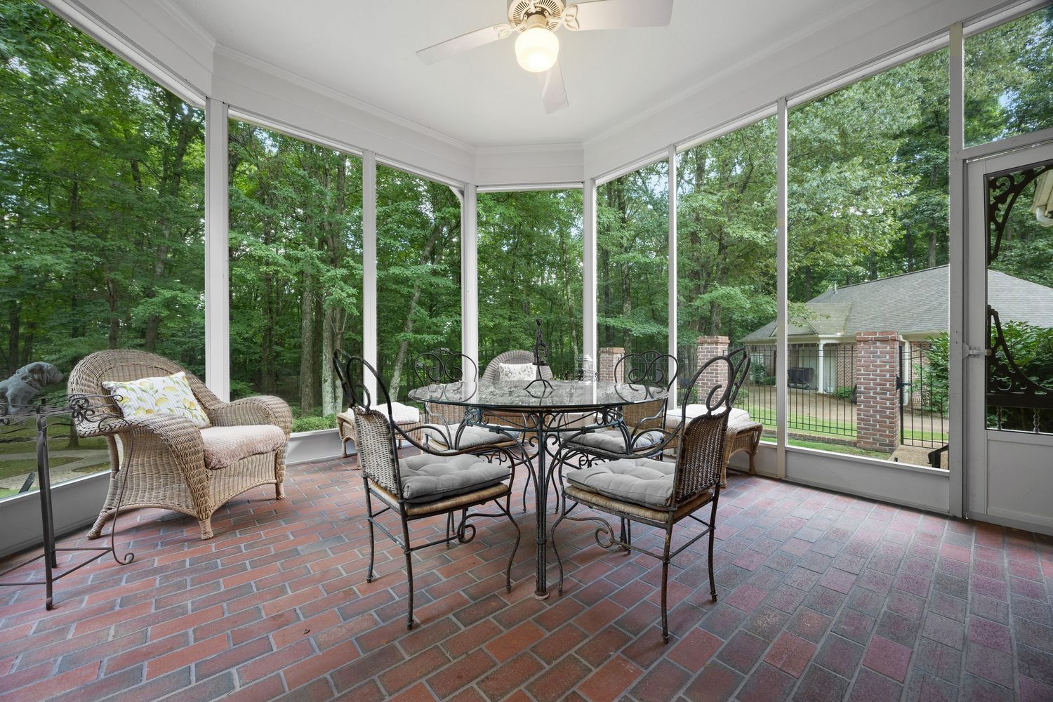 Enclosed porch with brick flooring and comfortable seating overlooking lush green landscape.