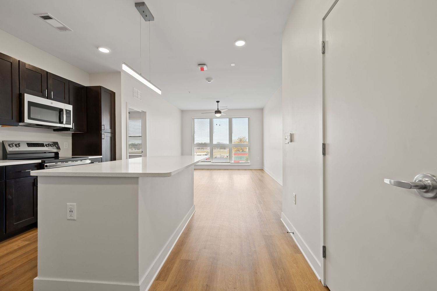 Modern apartment interior with white walls, hardwood floors and recessed lighting in a long hallway.
