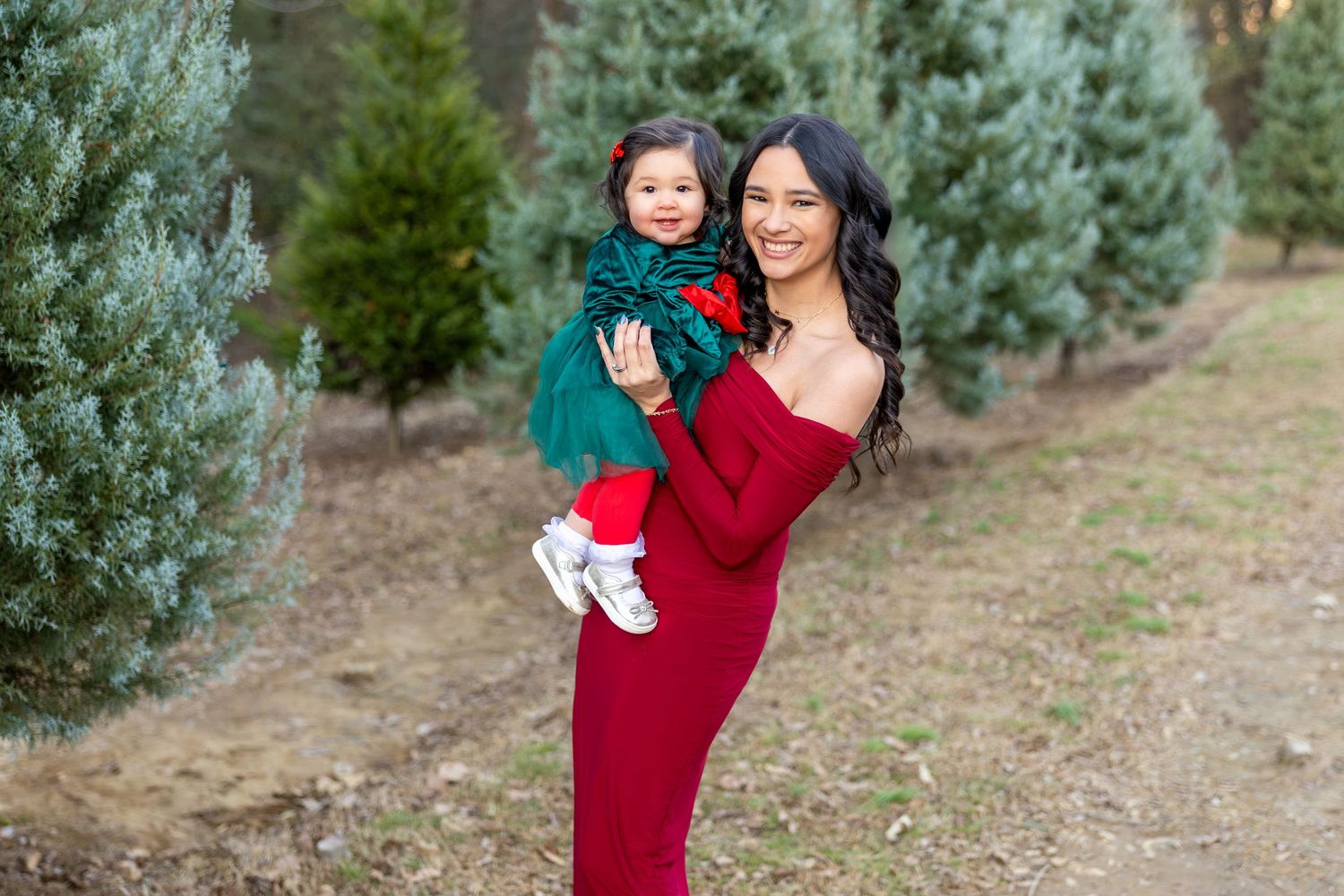 Family wearing red and teal outfits poses together among evergreen trees during an outdoor photo session.
