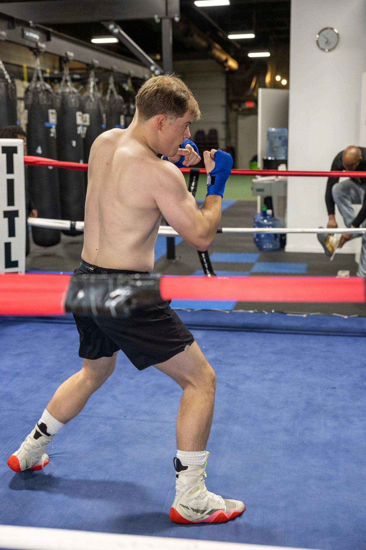 Shirtless boxer training in fighting stance on blue boxing ring mat.