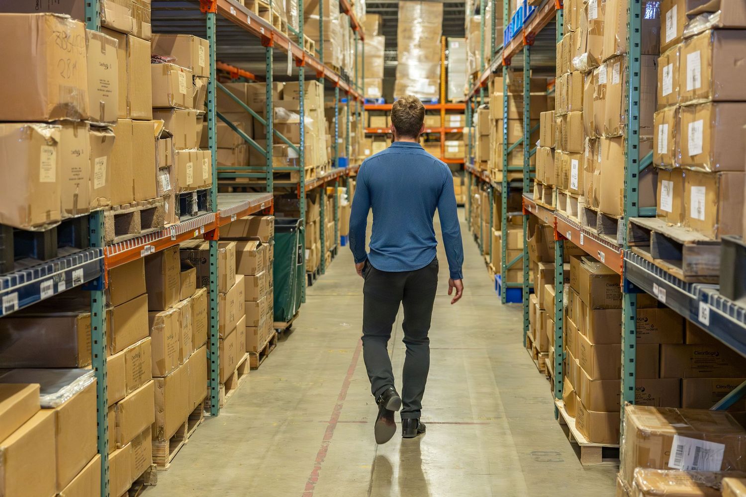 Large warehouse interior with tall storage racks filled with cardboard boxes and inventory.