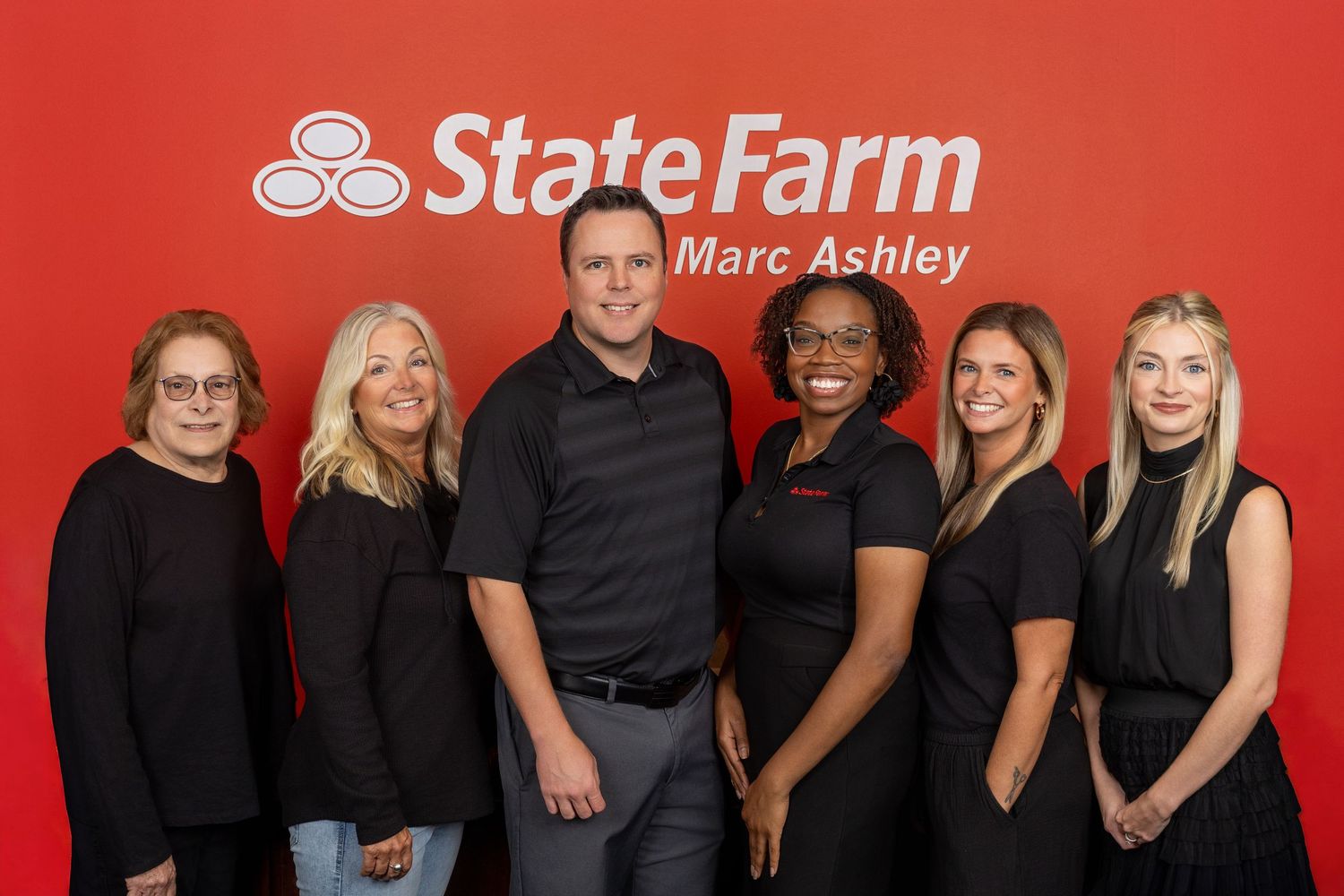 Insurance office team posing in front of red State Farm logo wall.