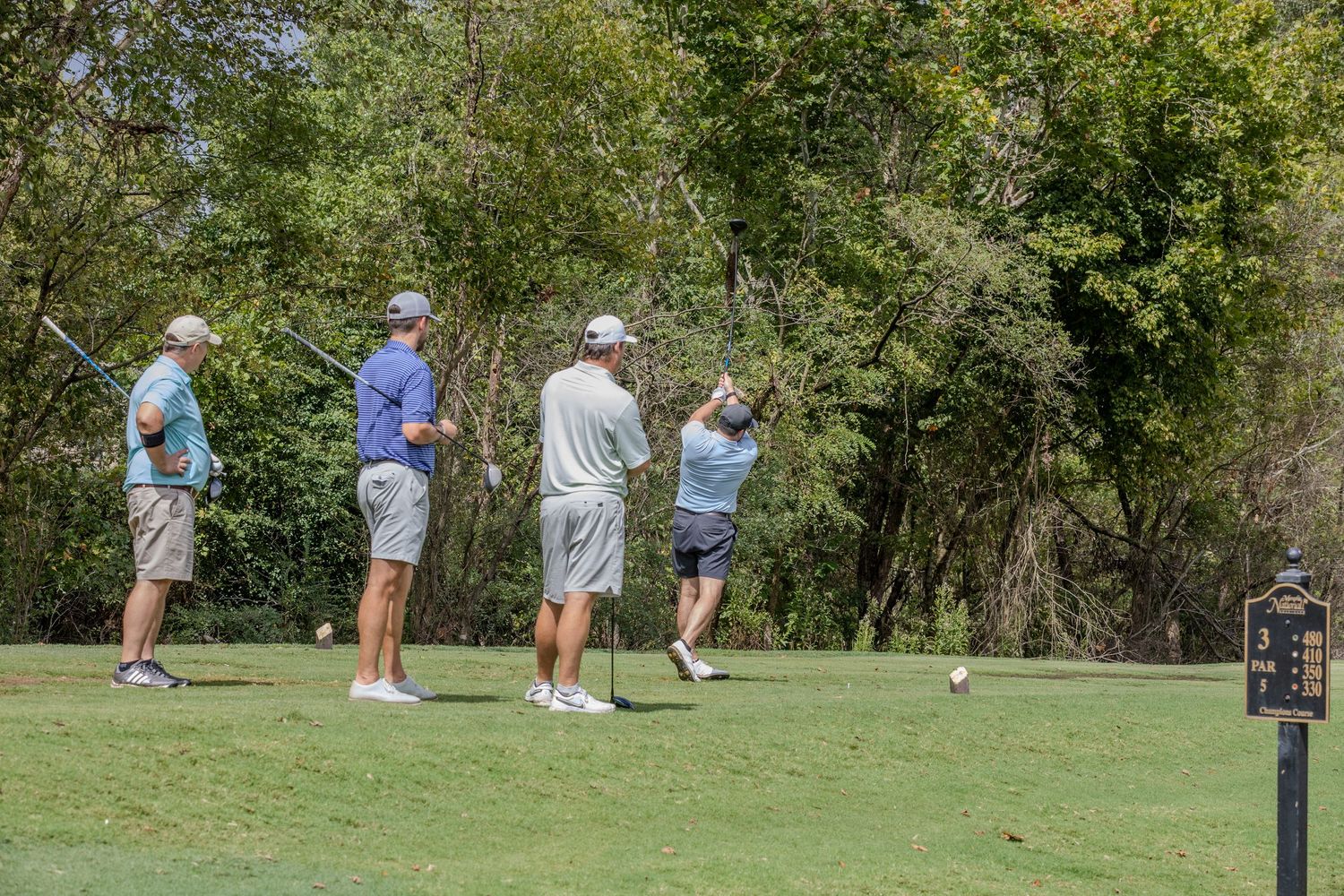 Group of golfers gathered on a scenic golf course with trees in the background.