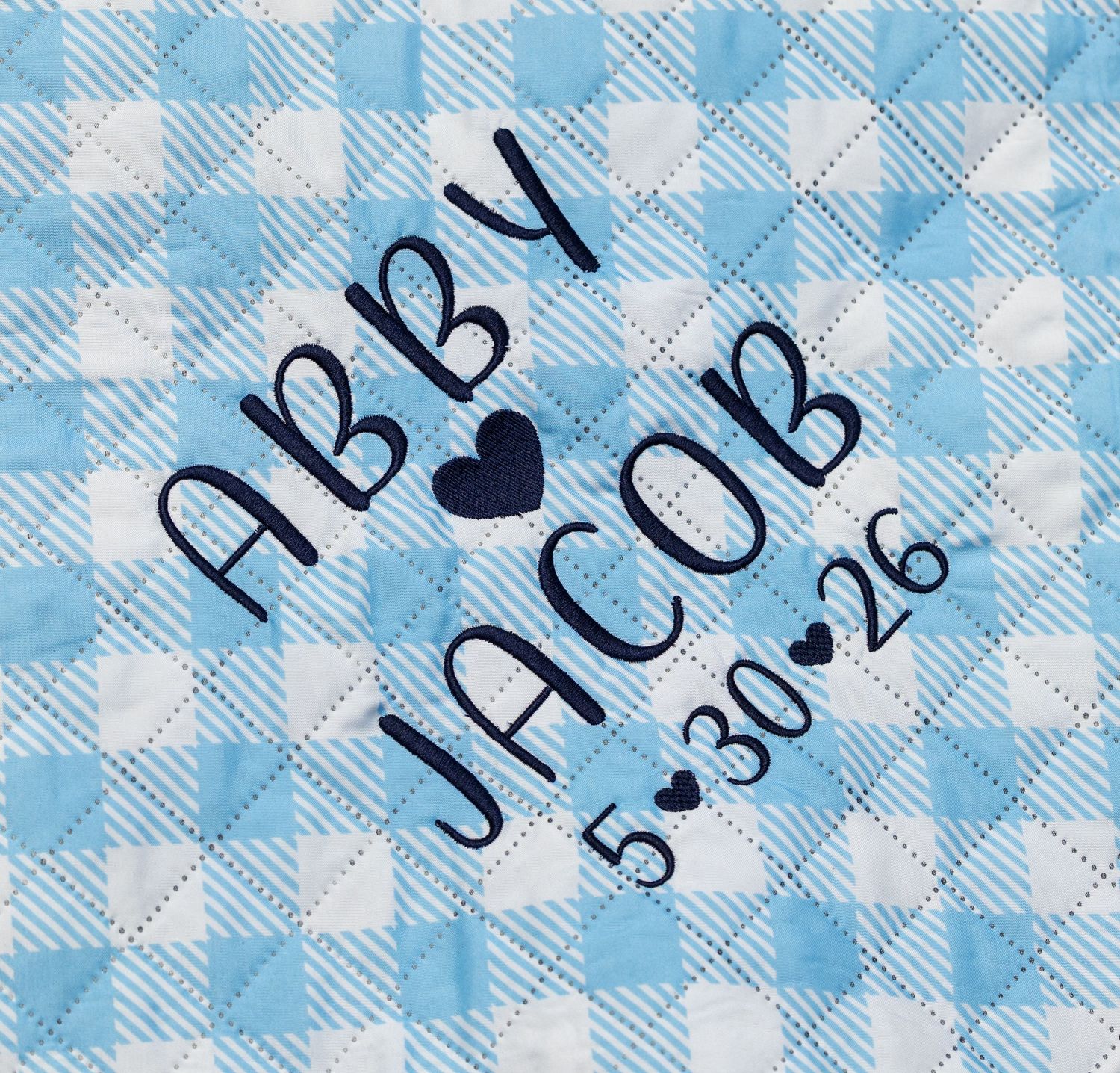 Blue gingham quilted fabric with embroidered names Abby and Jacob with date 5-30-26 in navy blue thread.