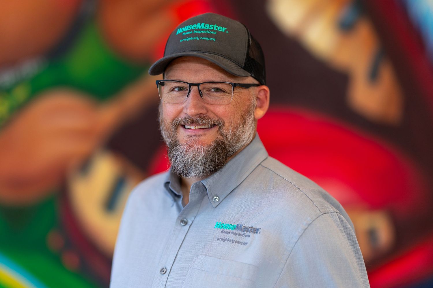 Smiling man with beard and glasses wearing a gray ServiceMaster uniform shirt and black cap.