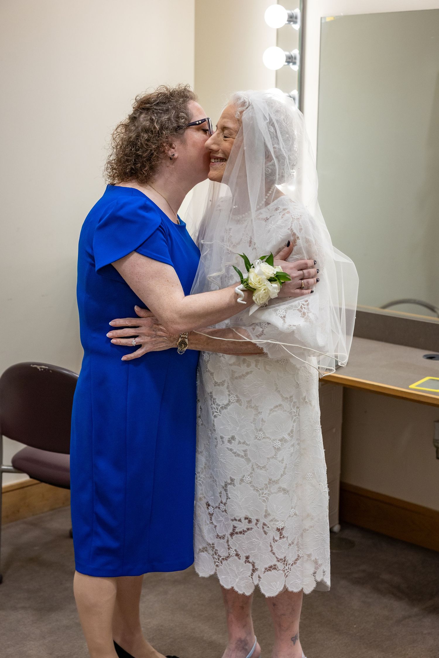 A heartwarming embrace between two people, one in a white lace dress and veil, the other in royal blue.