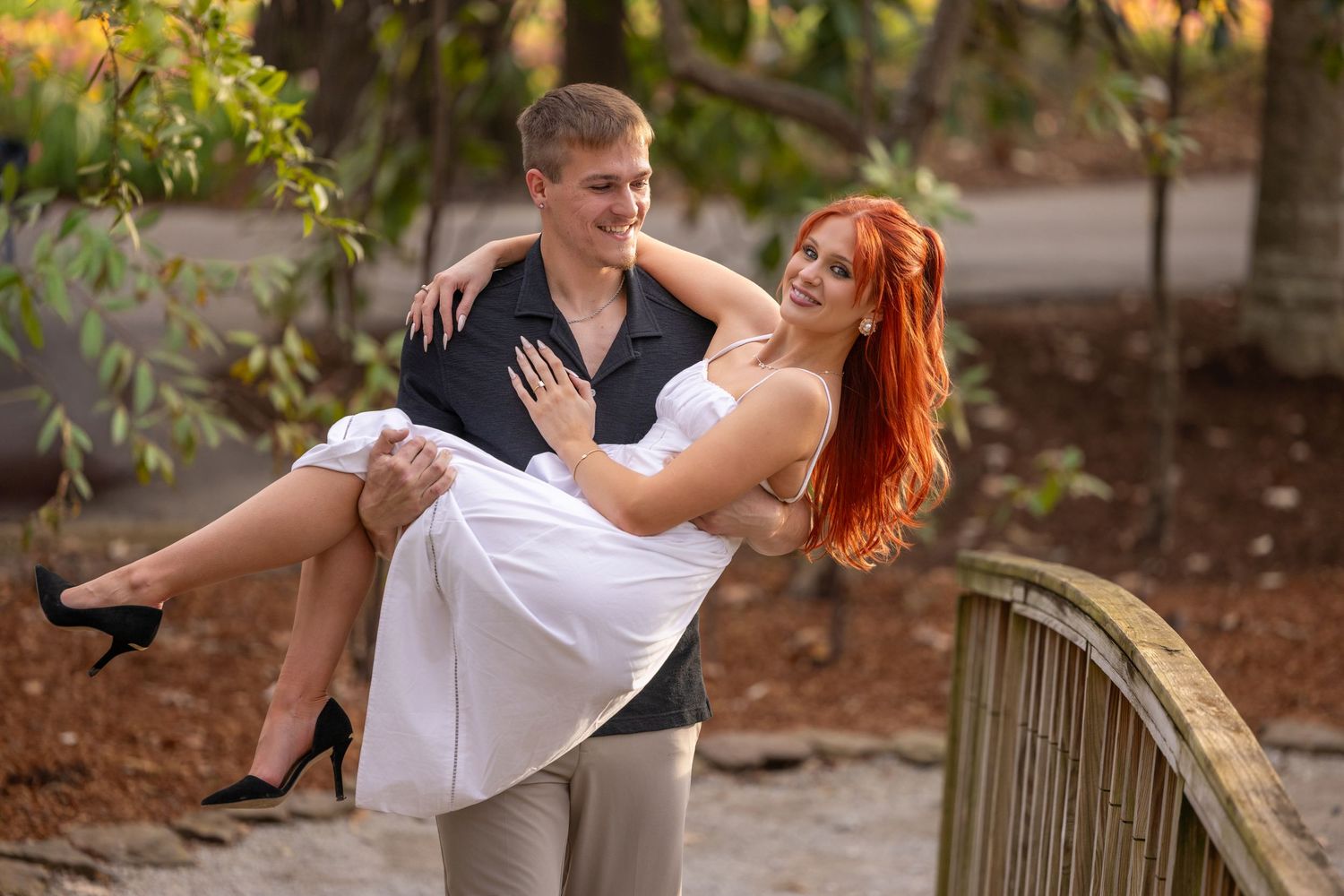 A couple in formal attire dances together on a wooden bridge in a romantic outdoor setting.