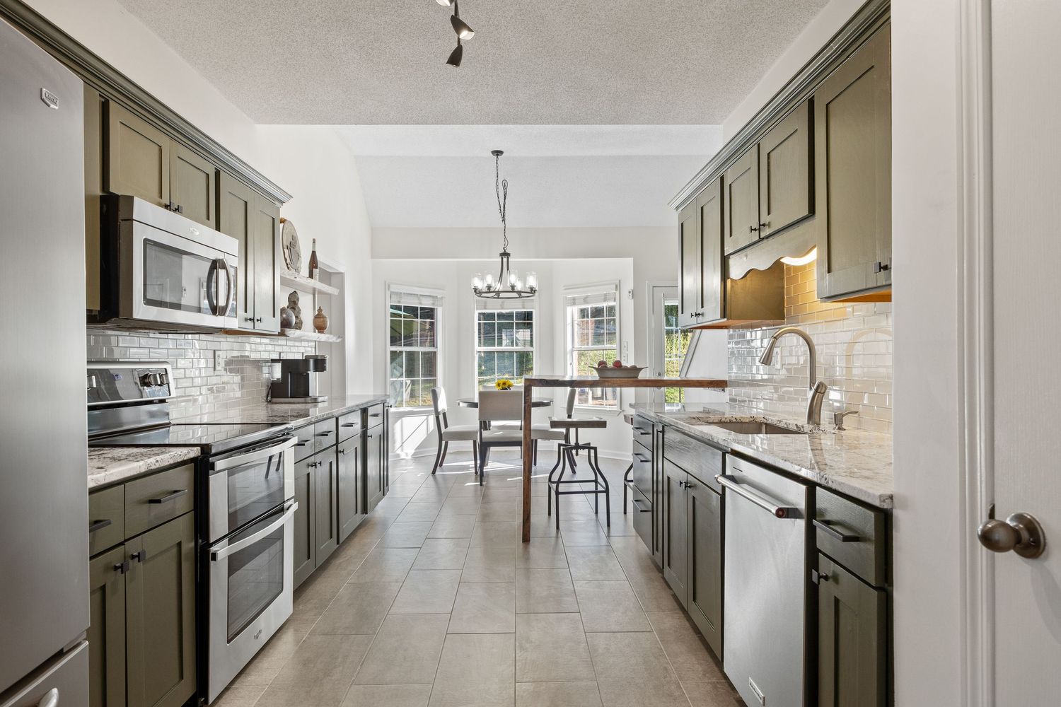 Modern open concept kitchen and living area with white walls, dark cabinets and pendant lighting in luxury apartment interior.