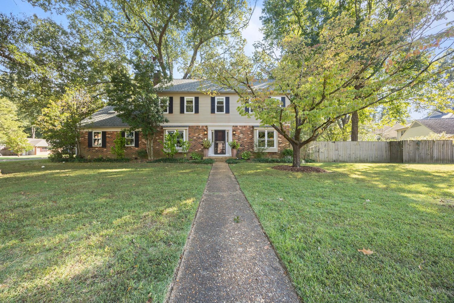 Long stone walkway leads through a green lawn to a traditional brick house on a sunny day.