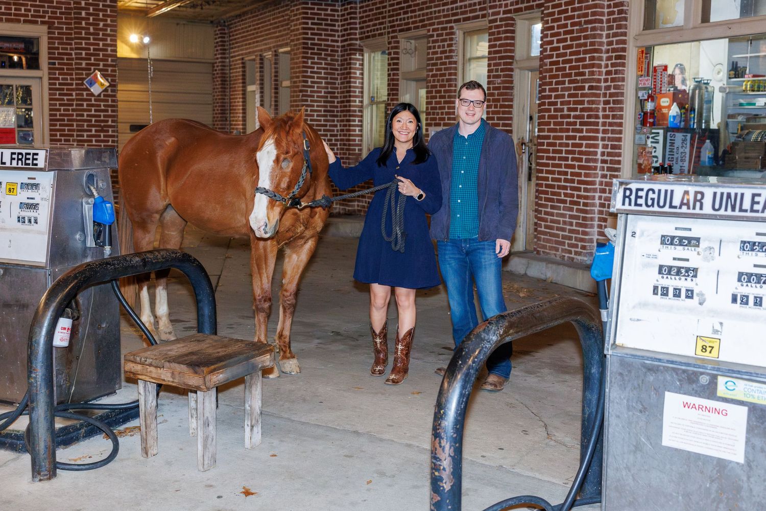 Long view of a brick stable interior with horses and posted signs.