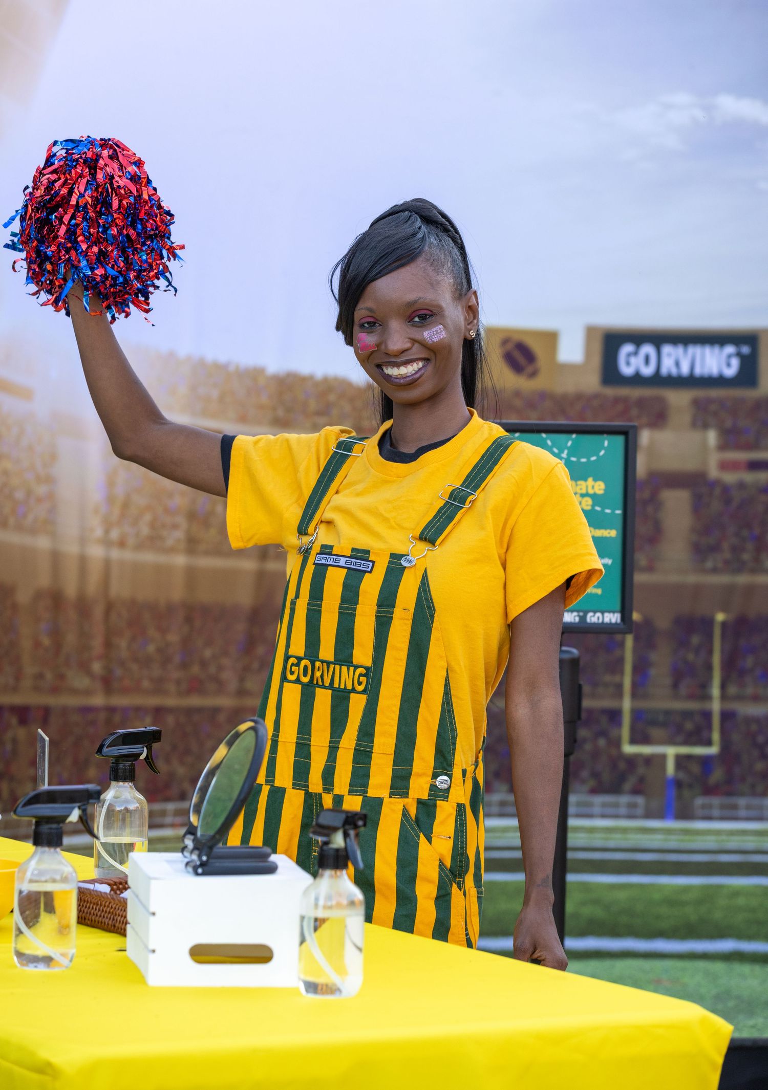 Cheerleaders in yellow and green striped uniforms perform at an outdoor sporting event.