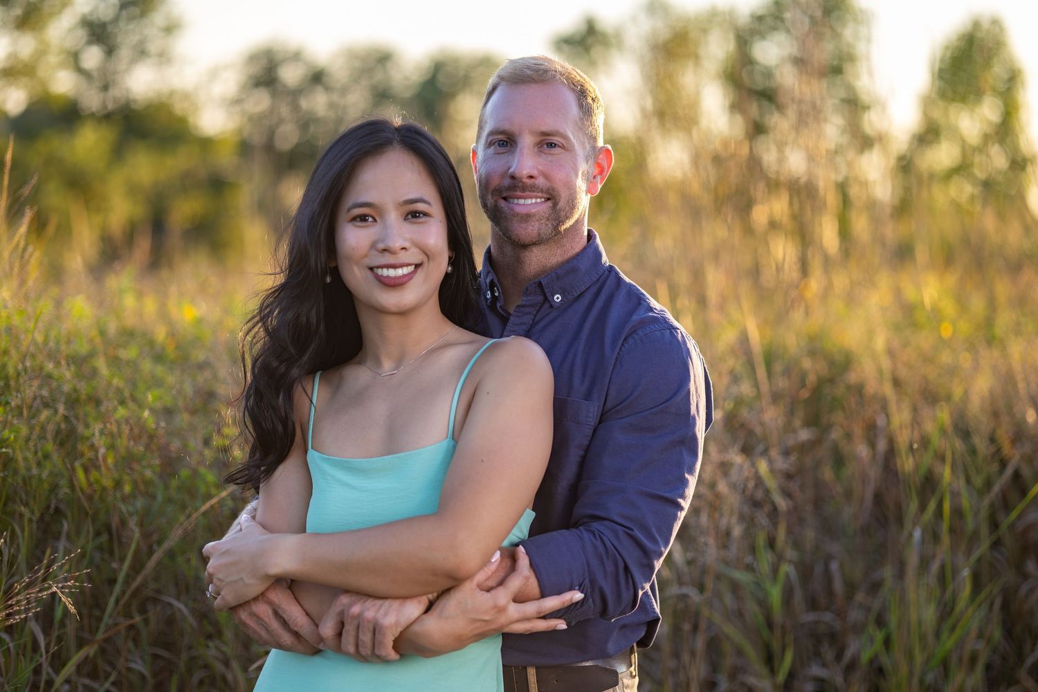 A couple poses together in a field during golden hour photography session.