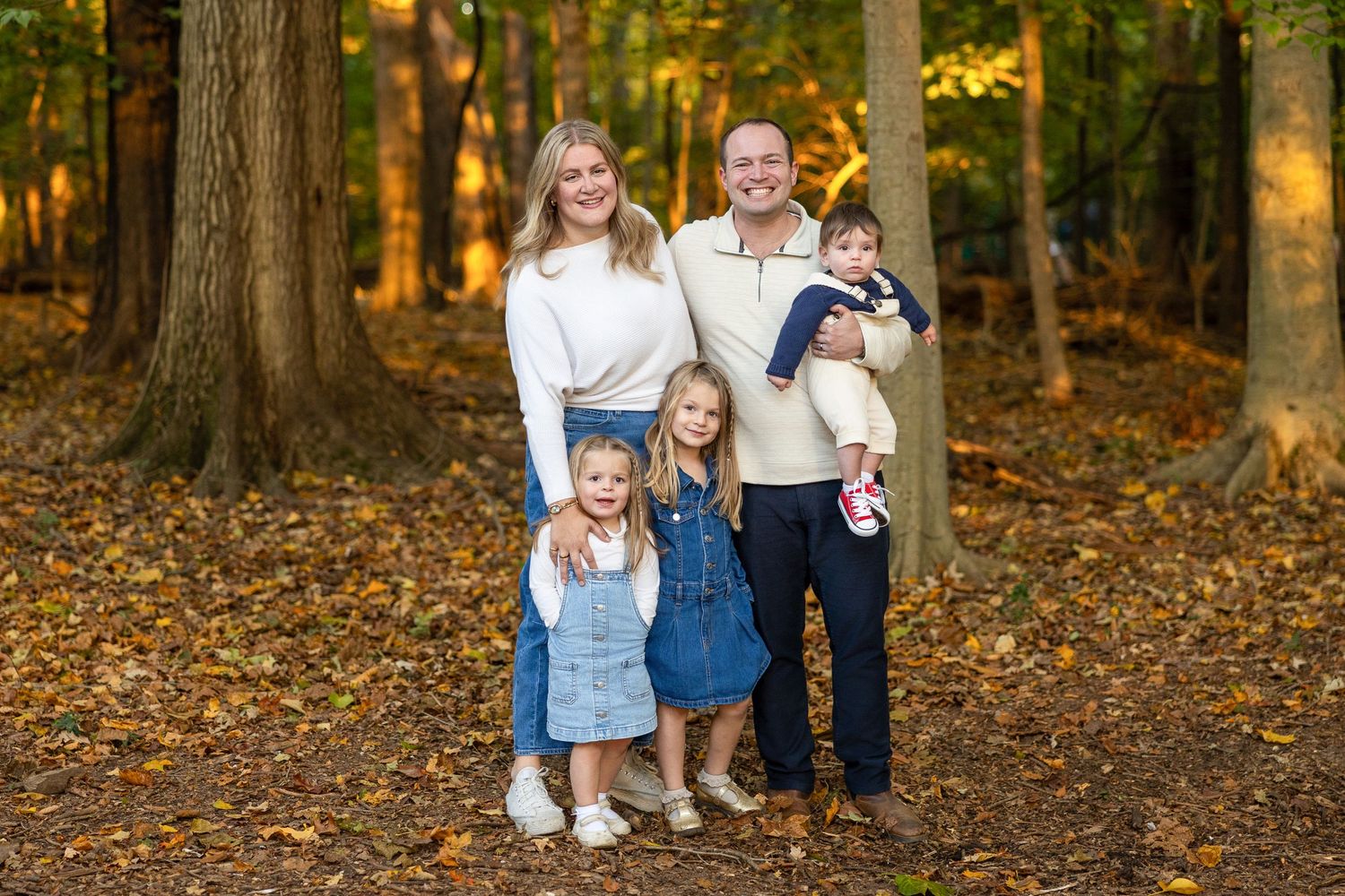 Autumn family photo session in a wooded area with fallen leaves.