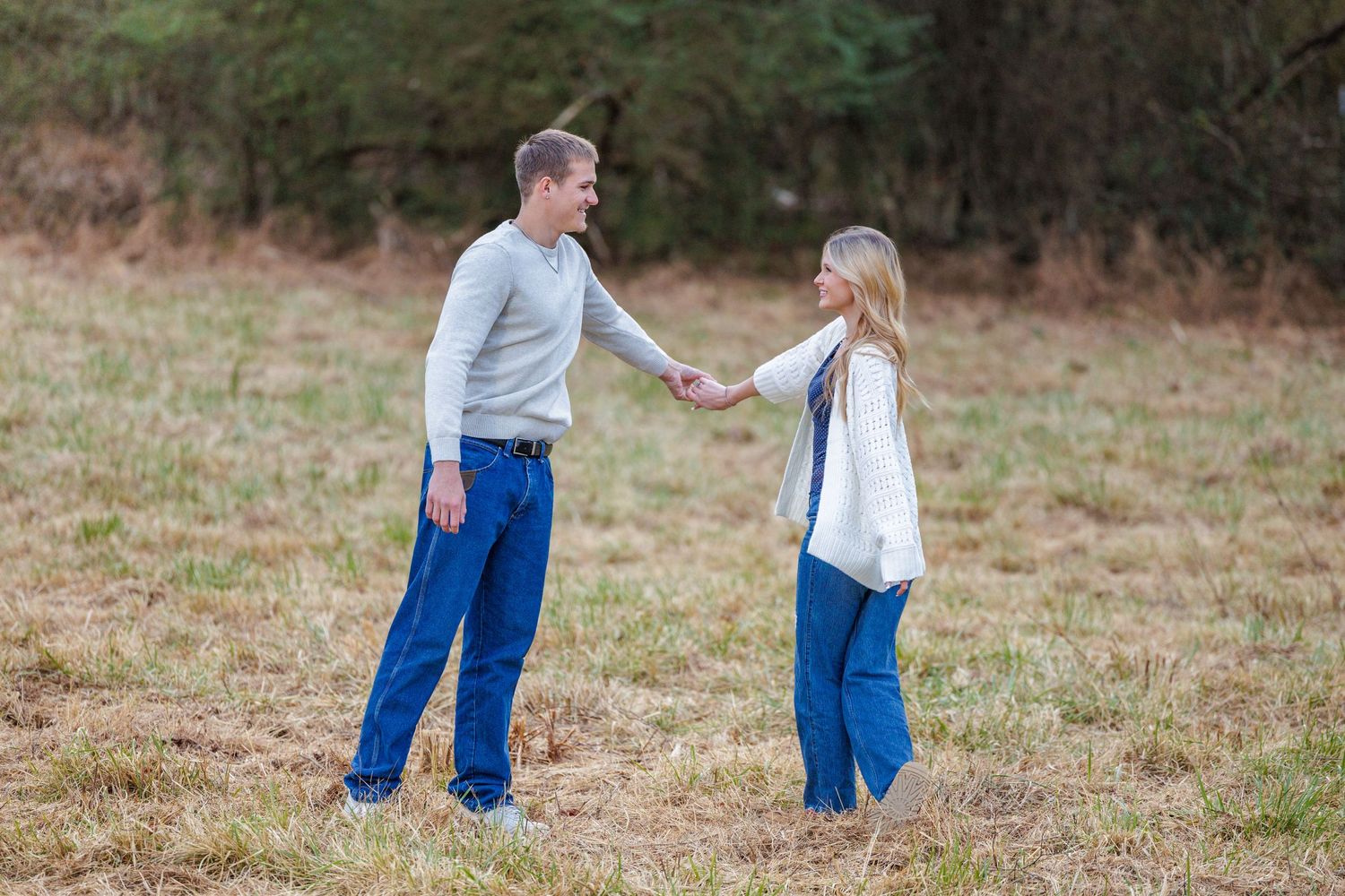 Four sequential images show a couple in blue jeans and white shirts walking through a grassy field together.