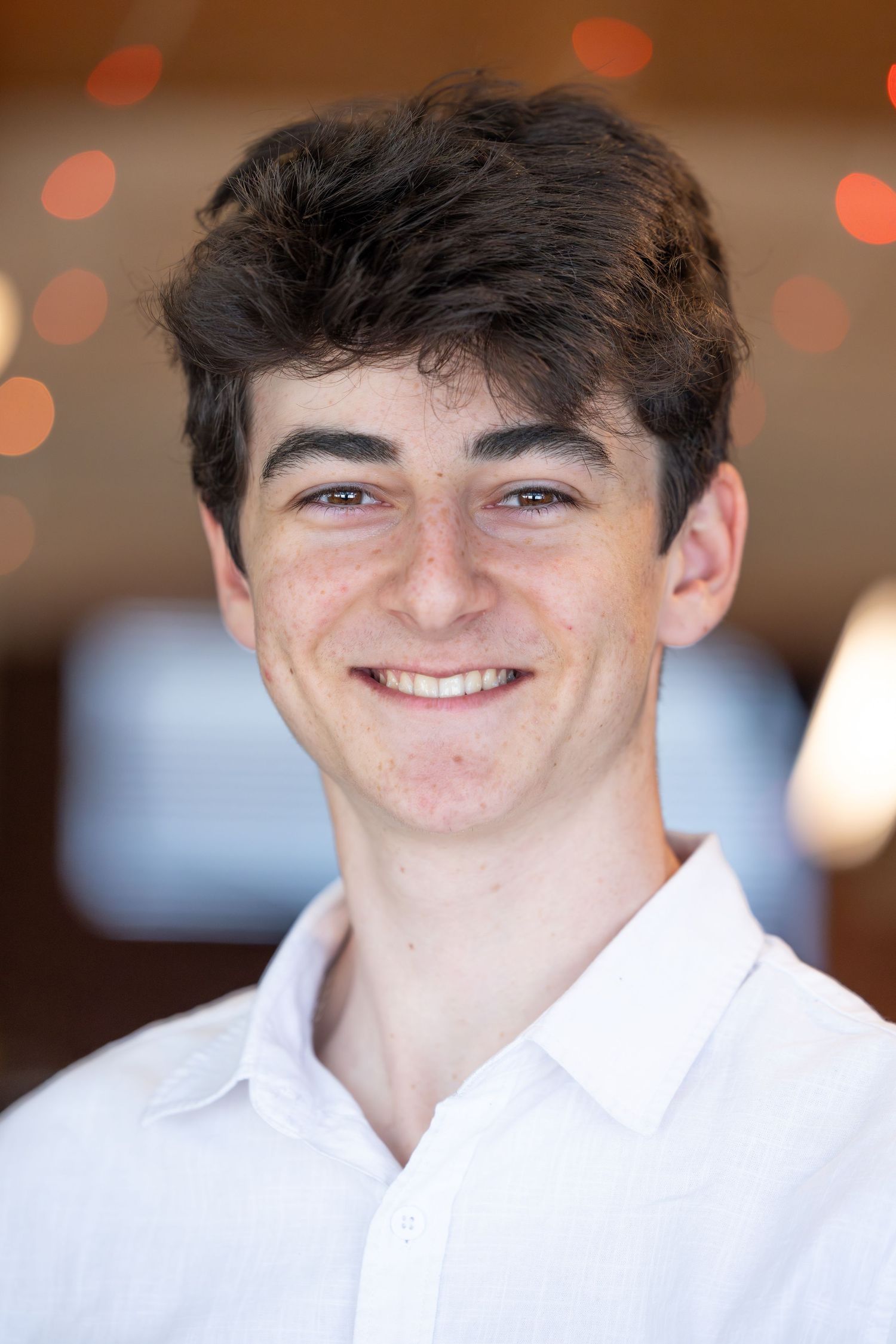 Smiling young man with dark hair wearing a white collared shirt, posed for a professional headshot photo.