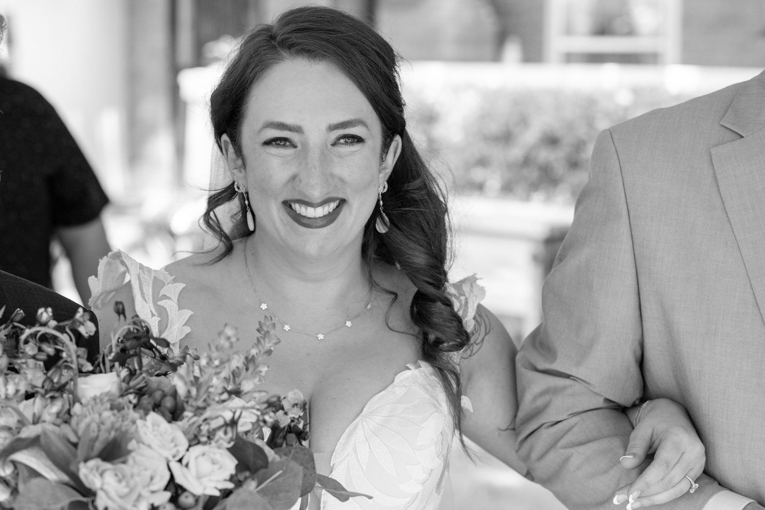 Smiling bride in white gown holding floral bouquet, black and white wedding portrait photo.
