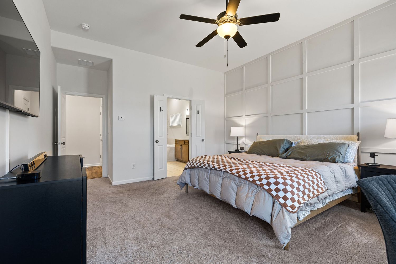 Modern master bedroom with chevron bedding, gray accent wall panels, plush carpet, and black ceiling fan.