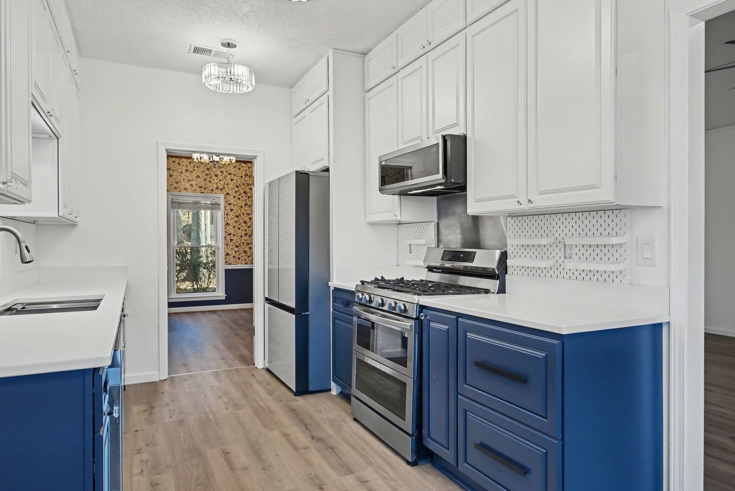 Modern galley kitchen with white upper cabinets, navy blue lower cabinets, stainless appliances and hardwood flooring.