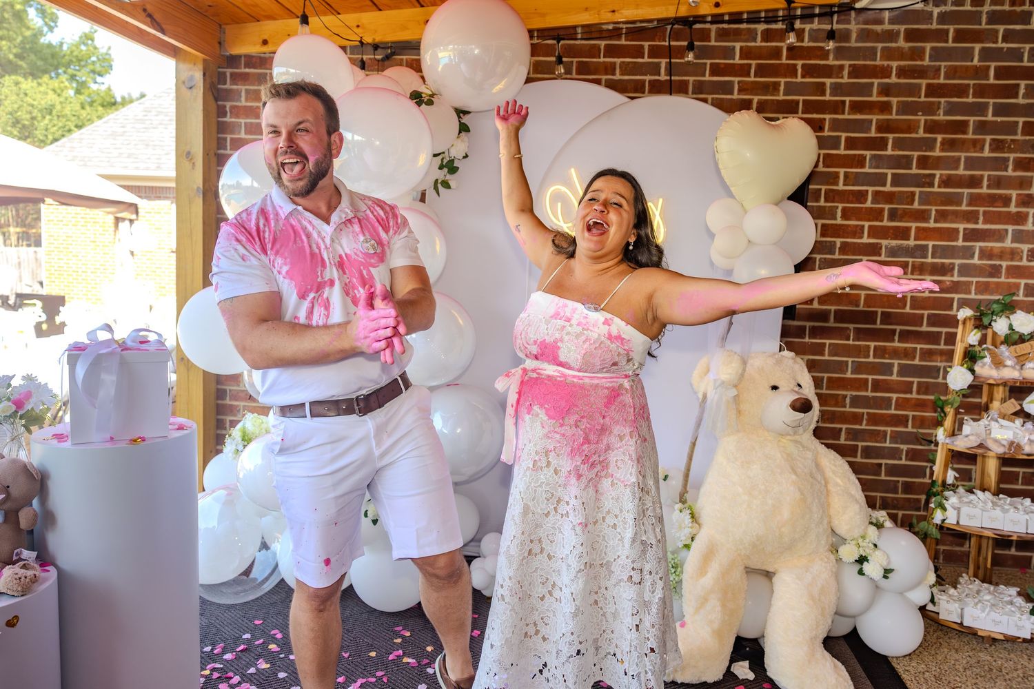 White balloons and decorations adorn a brick wall setting during a celebration.