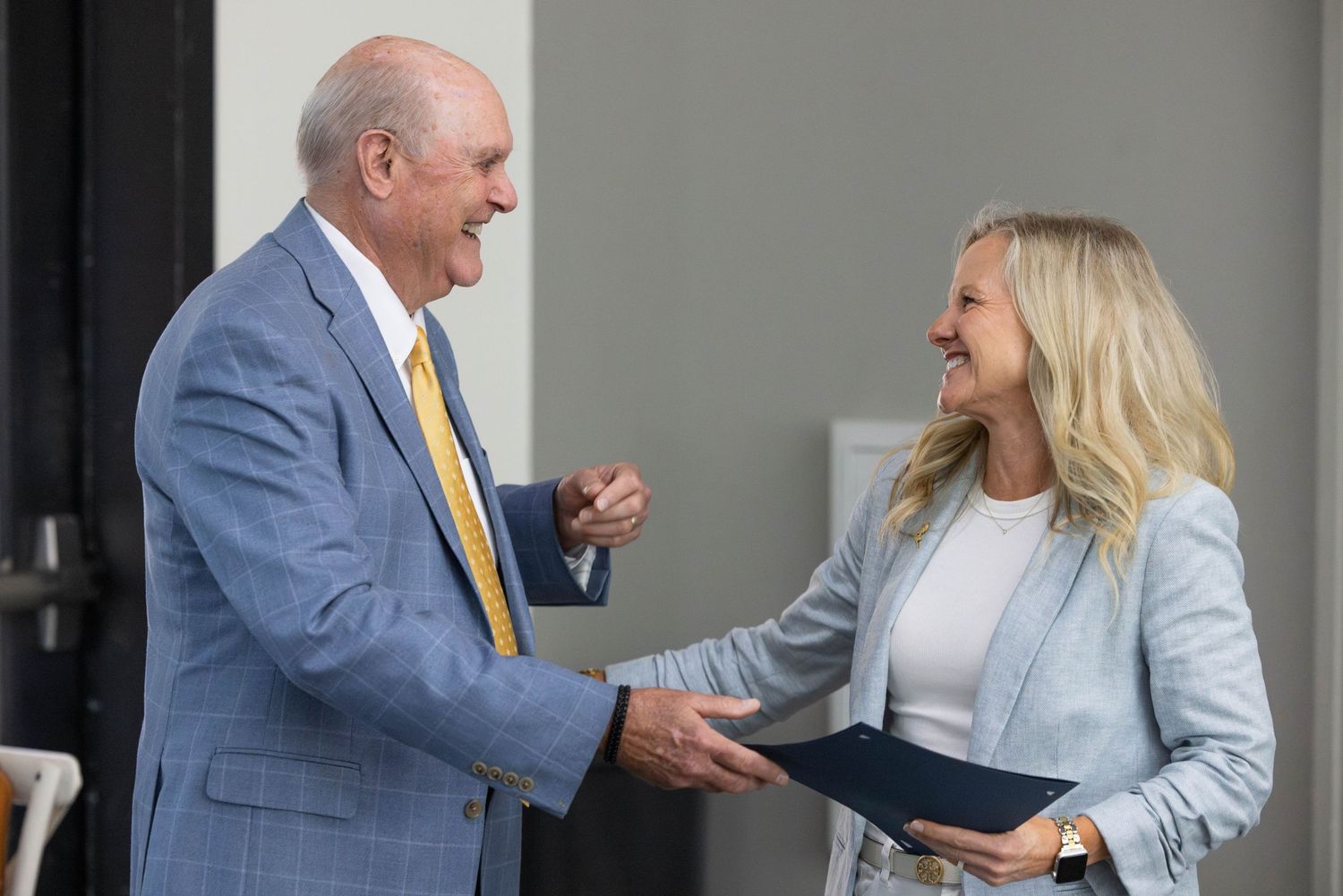 Business professionals in blue suits having an animated conversation in an office setting.