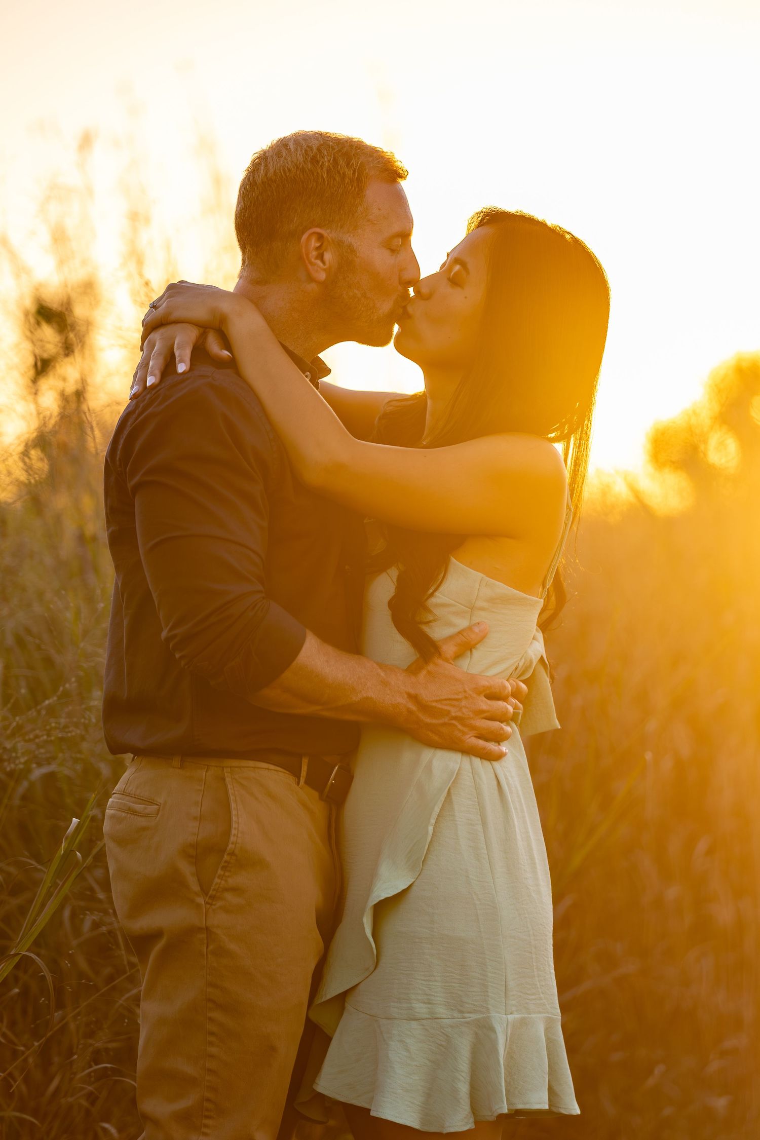 A couple shares an intimate moment at sunset in a field of tall grass.