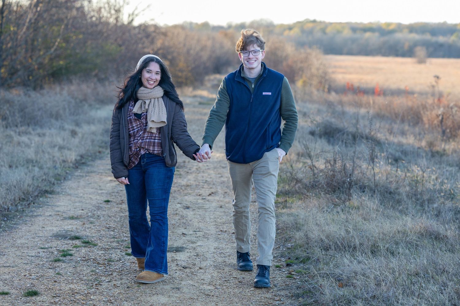 Couple walking hand in hand through a scenic autumn field after their engagement.