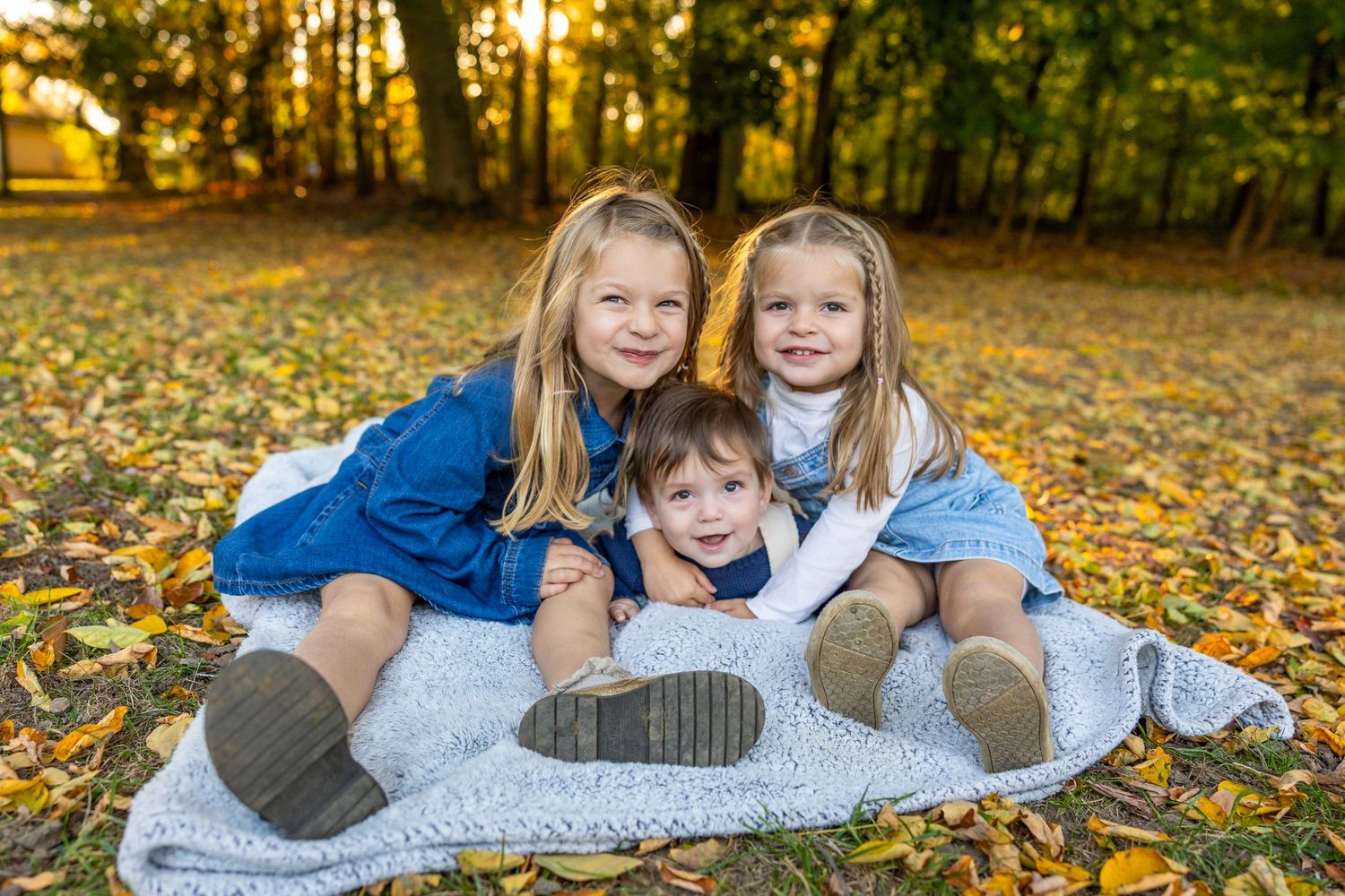 Children lying on gray blanket surrounded by fall foliage.