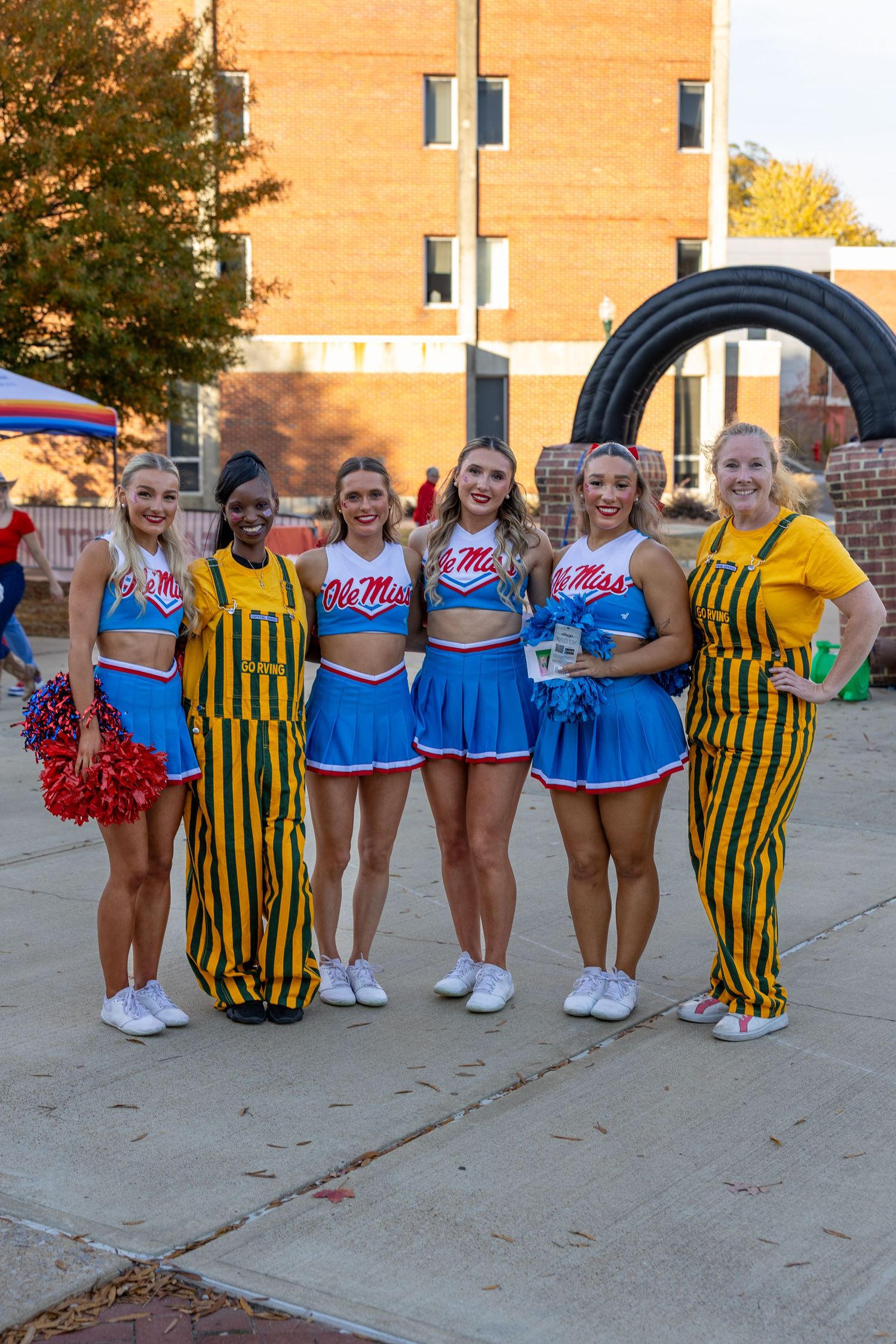 Cheerleaders and mascots in blue and yellow uniforms posing together outdoors.