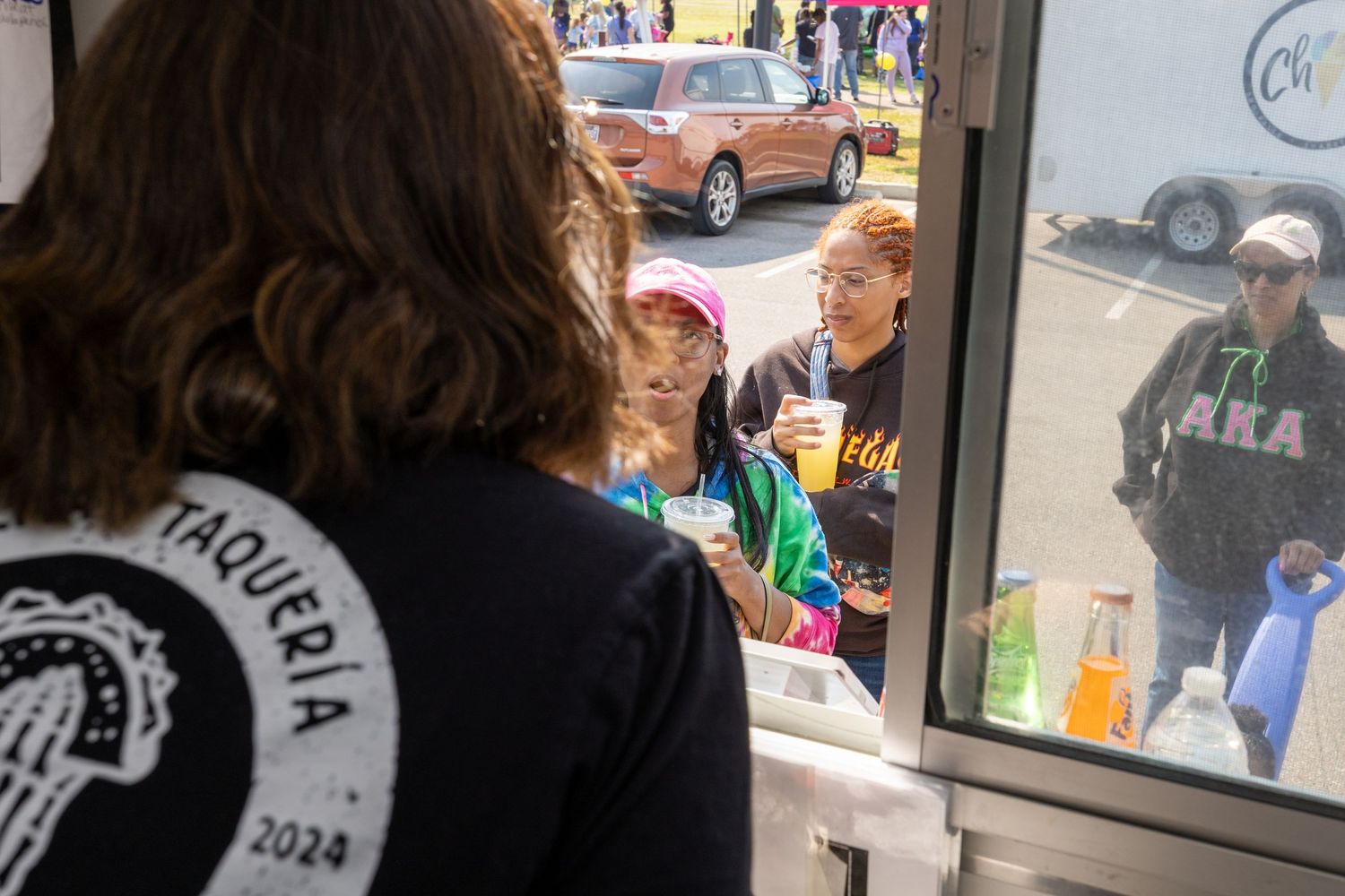 People gather at a food service window while someone wearing a black t-shirt takes orders from inside.