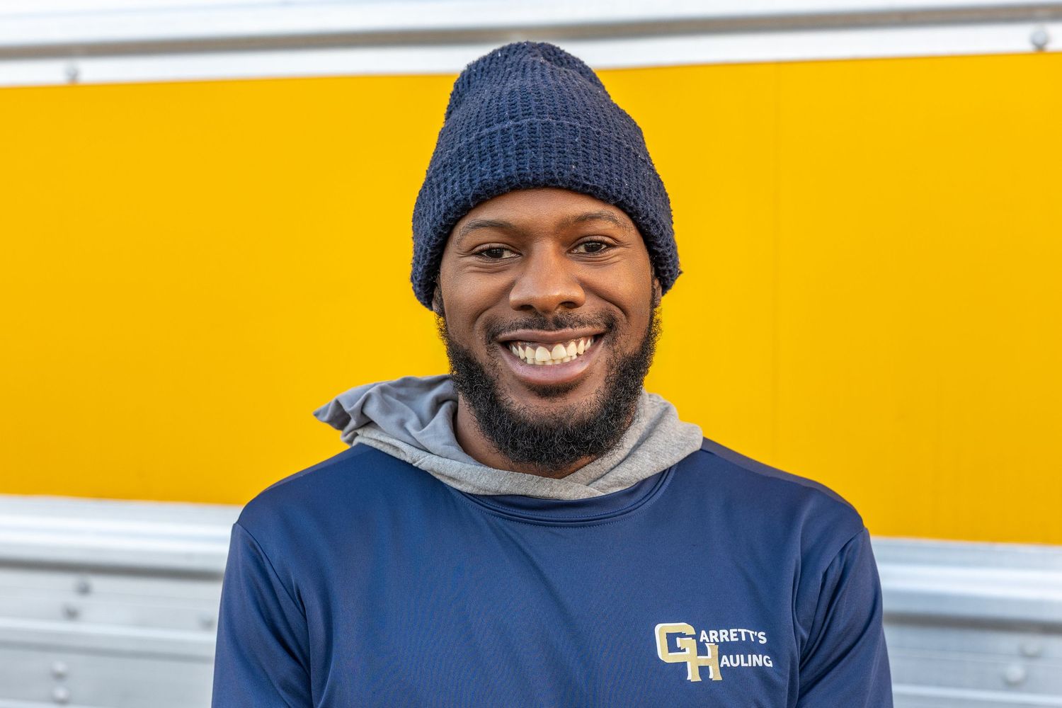 Employee wearing winter beanie and navy uniform smiling against yellow backdrop.
