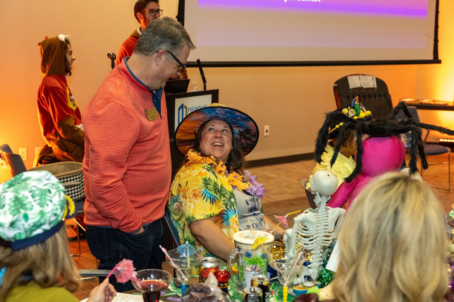 Attendees in costumes at a themed event with purple lighting and projection screens.