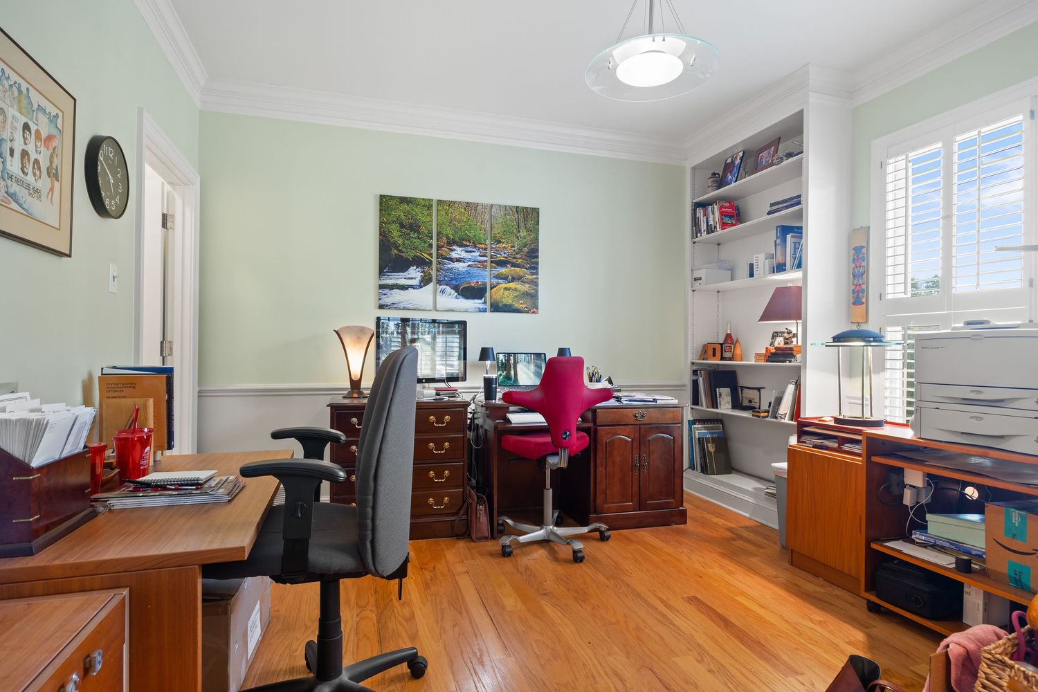 Modern home office with hardwood floors, white walls, and large windows showcasing natural light and minimalist decor.
